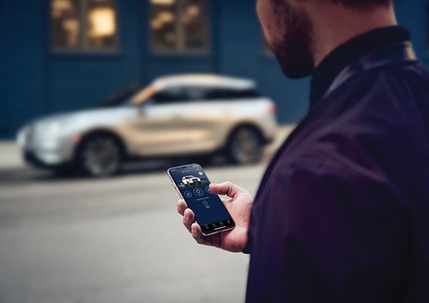 A person is shown interacting with a smartphone to connect to a Lincoln vehicle across the street. | Duncan Lincoln in Blacksburg VA